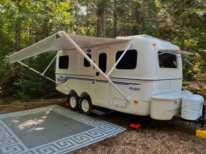 Enjoying the outdoors with an RV rental: a white Escape travel trailer set up at a wooded campsite with its awning extended.. Escape Trailer Escape Trailer Trailer 2022