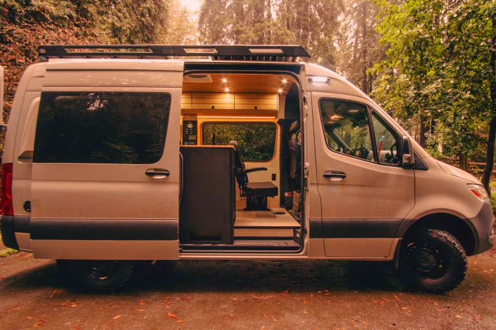 This light gray custom Sprinter camper van rv rental has an open side door, revealing a cozy, wood-paneled interior.. Mercedes-Benz Sprinter 2023