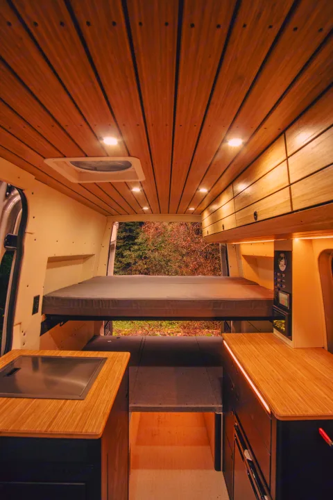 Modern bamboo-lined RV rental interior with a raised bed, integrated lighting, and full kitchen amenities.. Mercedes-Benz Sprinter 2023