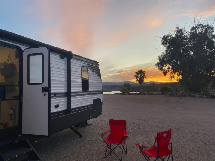 Peaceful RV rental evening: Sunset over mountains & lake, two chairs await by the camper.. Keystone RV Hideout 2022
