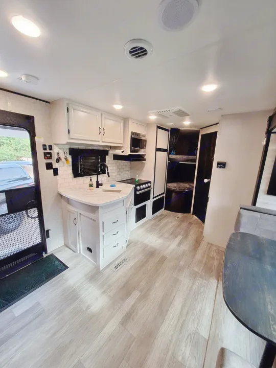 Modern RV rental interior: bright kitchen with white cabinets, light wood-look flooring, and a bunk bed area.. Jayco Jay Flight 2022