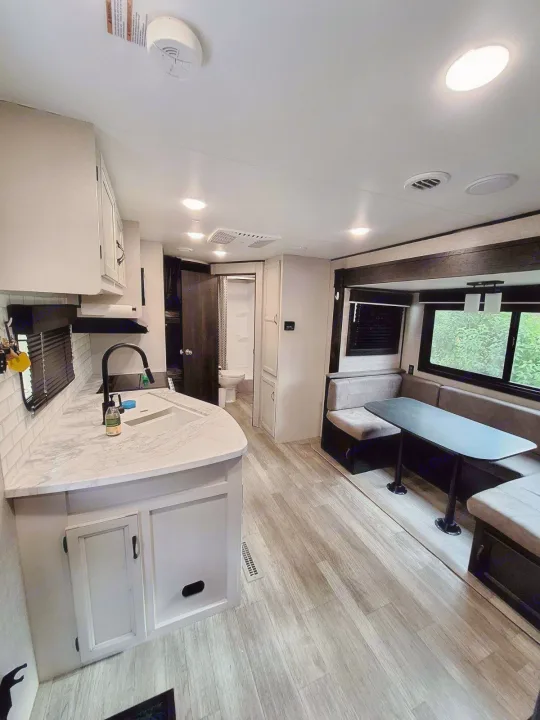Spacious RV rental interior featuring a modern kitchen, U-shaped dinette, and visible bathroom. Light wood flooring.. Jayco Jay Flight 2022