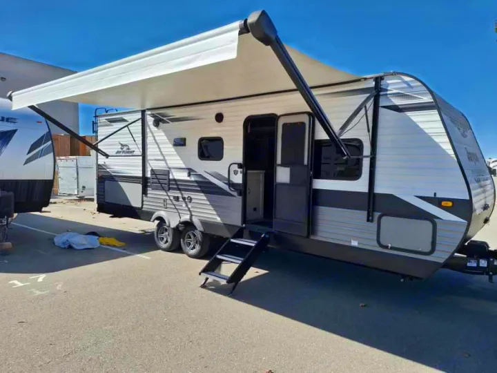 A Jay Flight travel trailer, perfect for RV rental adventures, with its awning extended and entry steps down, parked outdoors.. Jayco Jay Flight 2022