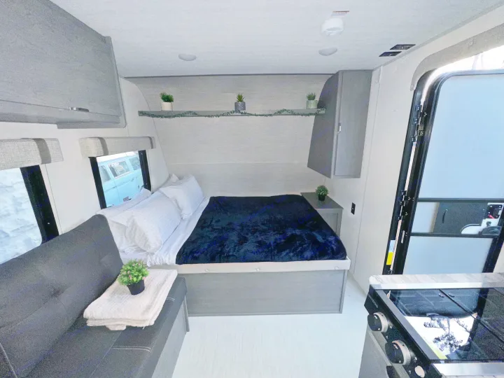 Interior of a modern RV rental, featuring a bed, a black sofa, and a compact kitchen area with a stovetop.. Forest River Ozark 2024