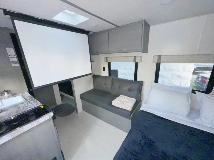 RV rental interior featuring a kitchen, cozy bed, sofa, and a large projector screen for entertainment.. Forest River Ozark 2024