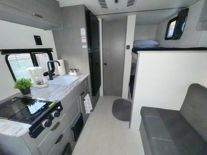 Modern RV rental interior: compact kitchen (stove, sink), fridge, bunks, and sofa in a sleek gray design.. Forest River Ozark 2024