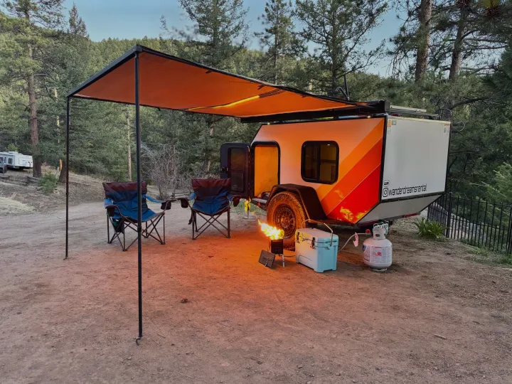 Camping with a vibrant teardrop rv rental, featuring an illuminated awning, chairs, a cozy fire, and cooler.. Custom Retro 2023