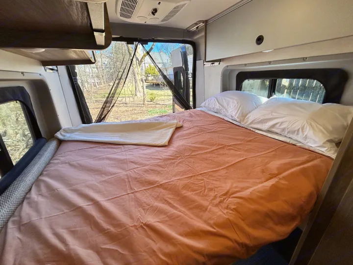 This RV rental offers a spacious bed and an immersive outdoor view from the open rear doors, complete with a bug screen.. Winnebago Solis 2023