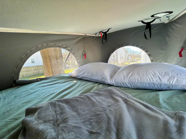Cozy sleeping area in an RV rental: a bed with pillows and blanket, and unique round tent windows.. Winnebago Solis 2023