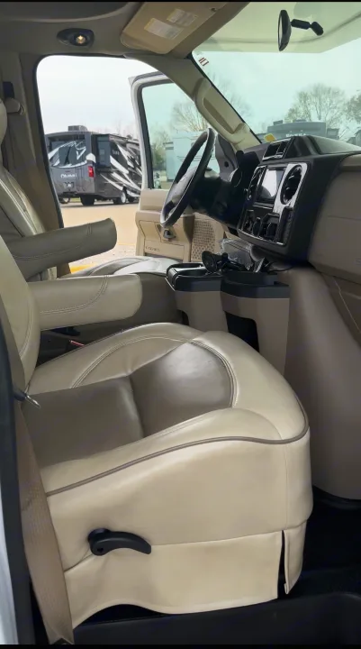 Inside an RV rental: light-colored leather front seats, armrests, and dashboard. Another RV is visible outside.. Jayco Greyhawk 2019