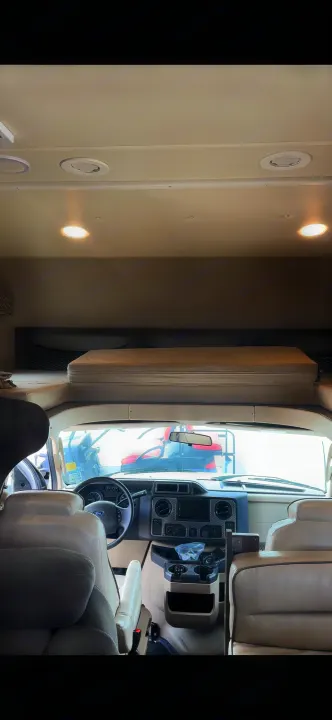 Interior of an RV rental showing the driver's cockpit and overhead bunk bed, perfect for travel accommodations.. Jayco Greyhawk 2019