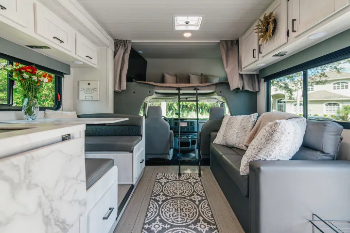 Explore this spacious RV rental interior, featuring a comfortable dinette, plush sofa, and convenient overhead bunk for all your travel adventures.. East to West Entrada 2024