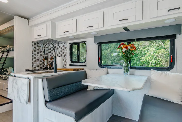 This modern RV rental interior features a functional kitchen, dining booth, and cozy bunk beds, perfect for family adventures.. East to West Entrada 2024