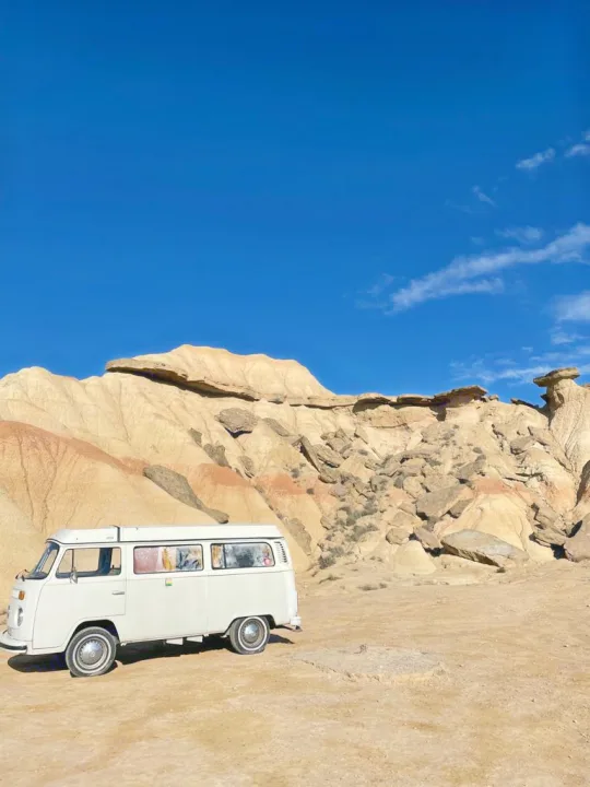 A classic white VW camper van, ideal for your next RV rental adventure, parked in a desert landscape with unique rock formations.. Volkswagen T2 1978