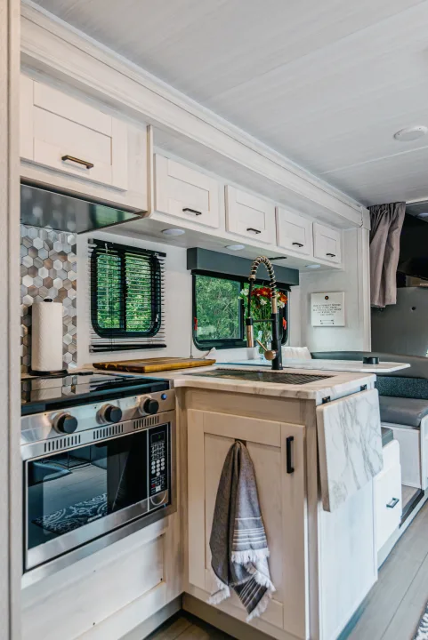 Modern RV rental kitchen with stove, microwave, sink, and dining booth, ready for adventures.. East to West Entrada 2024