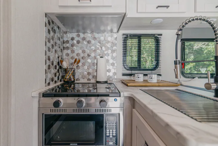Sleek RV kitchen interior featuring a stove, microwave, sink, and chic tile backsplash, ideal for your rv rental.. East to West Entrada 2024