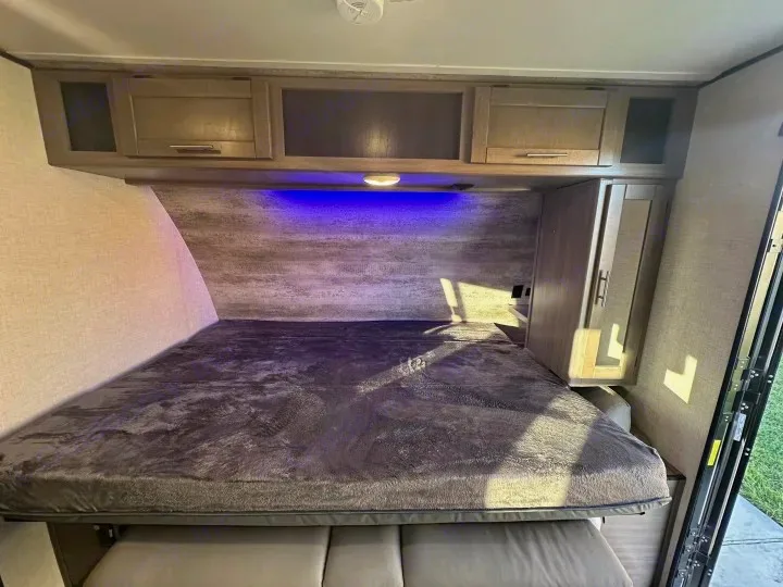 Experience a comfortable RV rental bedroom with a plush bed, overhead cabinets, blue lighting, and wardrobe storage.. Crossroads Sunset Trail Super Lite 2022