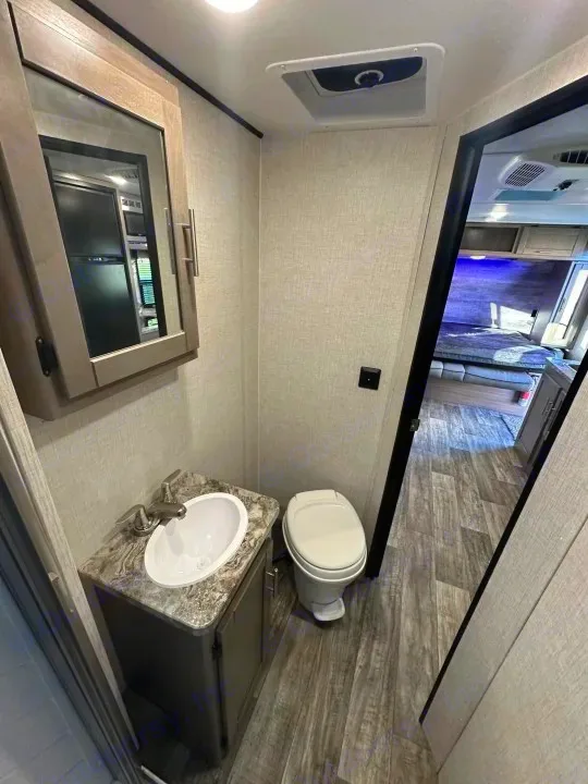 Compact RV rental bathroom: vanity, sink, toilet, and mirrored cabinet. A doorway reveals the bedroom. Efficient layout.. Crossroads Sunset Trail Super Lite 2022