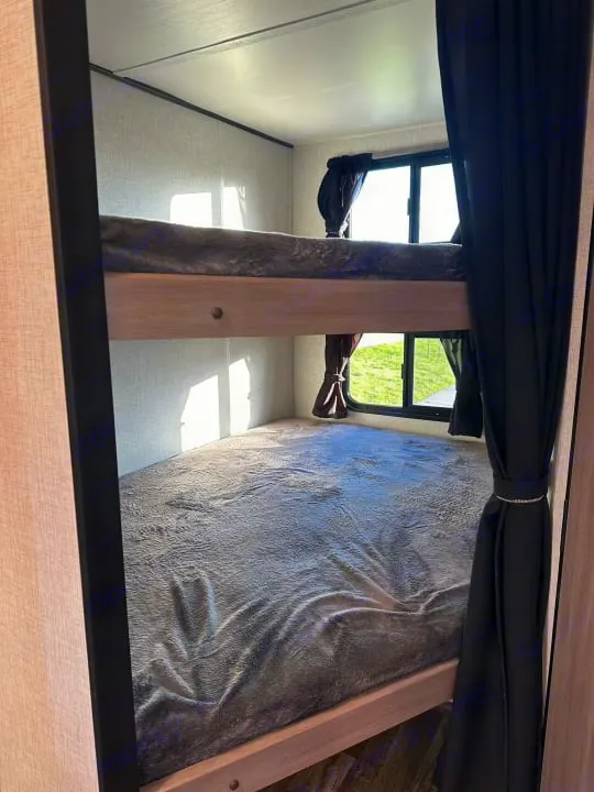 Inside an RV rental: two comfortable bunk beds with grey blankets and windows for natural light. Ideal for families.. Crossroads Sunset Trail Super Lite 2022
