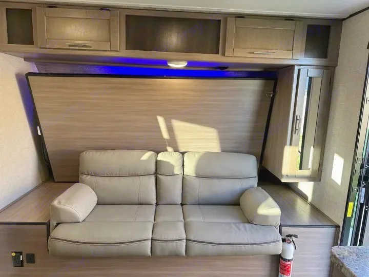 Inside this RV rental, find a light-colored sofa, overhead cabinets with blue lighting, and a wall panel that may conceal a bed.. Crossroads Sunset Trail Super Lite 2022