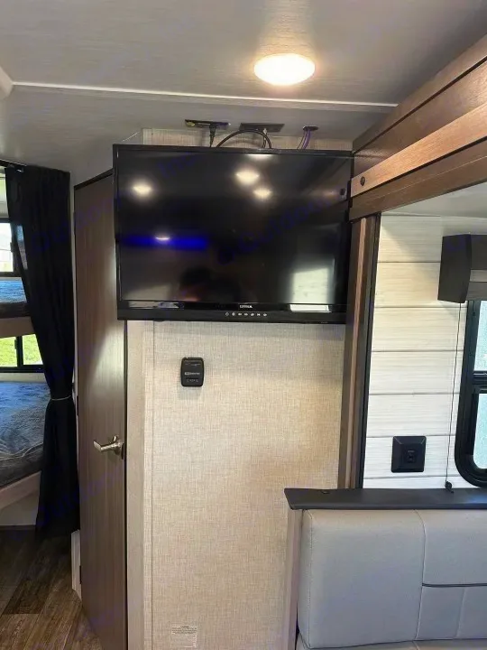 RV rental living area. Enjoy a wall-mounted TV, thermostat, and comfy dinette, with bunk beds visible beyond.. Crossroads Sunset Trail Super Lite 2022