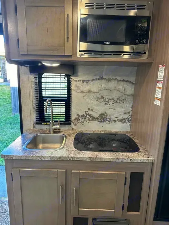This RV rental kitchenette features a compact sink, 2-burner stove, microwave, and ample cabinets for on-the-go living.. Crossroads Sunset Trail Super Lite 2022