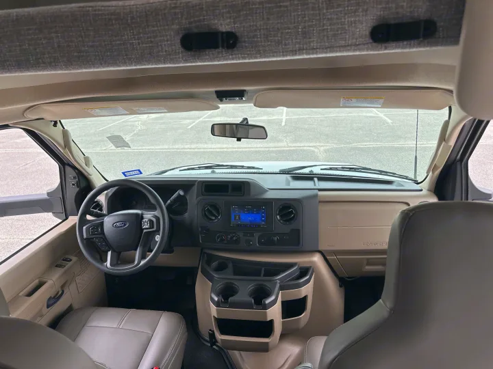 Inside an RV rental: View of the spacious driver's area with dashboard, Ford steering wheel, seats, and overhead bunk.. Thor Quantum LC 2024