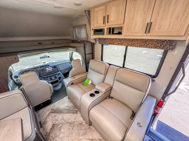Inside a modern RV rental, featuring a front cockpit, over-cab bunk, beige recliners, and wooden cabinets for travel comfort.. Forest River Sunseeker 2021
