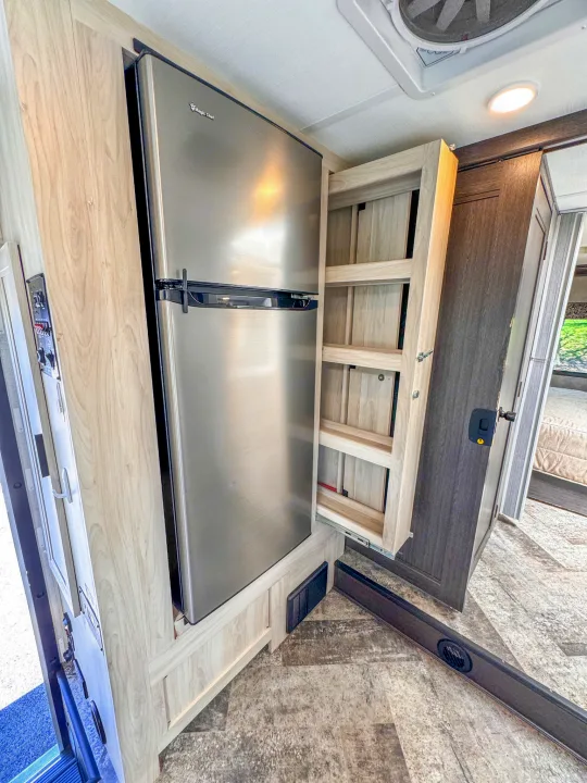 RV rental: Stainless steel refrigerator and pull-out pantry in a wood-paneled interior, revealing clever storage.. Forest River Sunseeker 2021