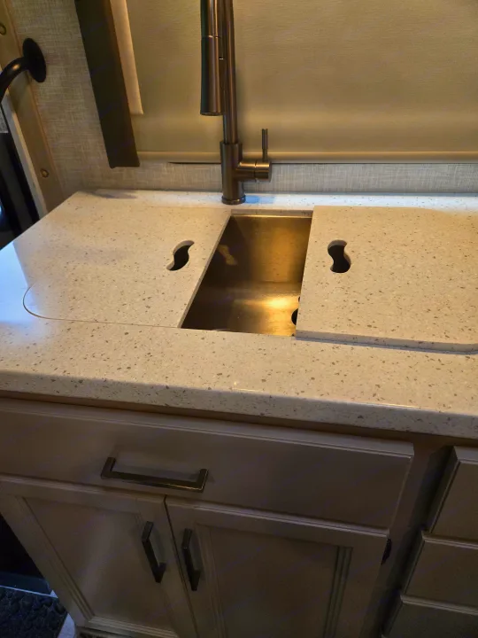 RV rental kitchen featuring a modern stainless steel sink, pull-down faucet, and custom solid-surface countertop covers.. Thor Quantum 2023