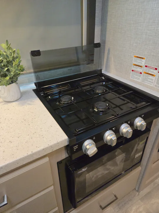 RV rental kitchen setup: black gas cooktop with glass cover, oven, and light speckled countertop for road cooking.. Thor Quantum 2023