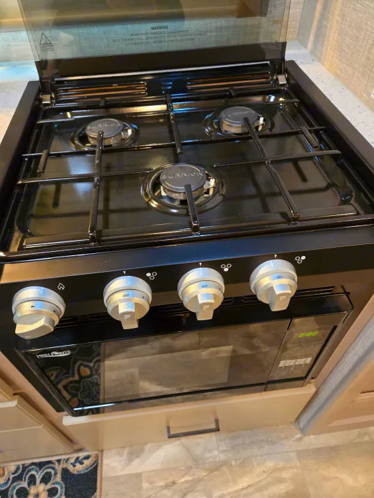 RV rental kitchen: a compact black Furrion gas stovetop with four burners and glass cover, plus a High Pointe microwave.. Thor Quantum 2023