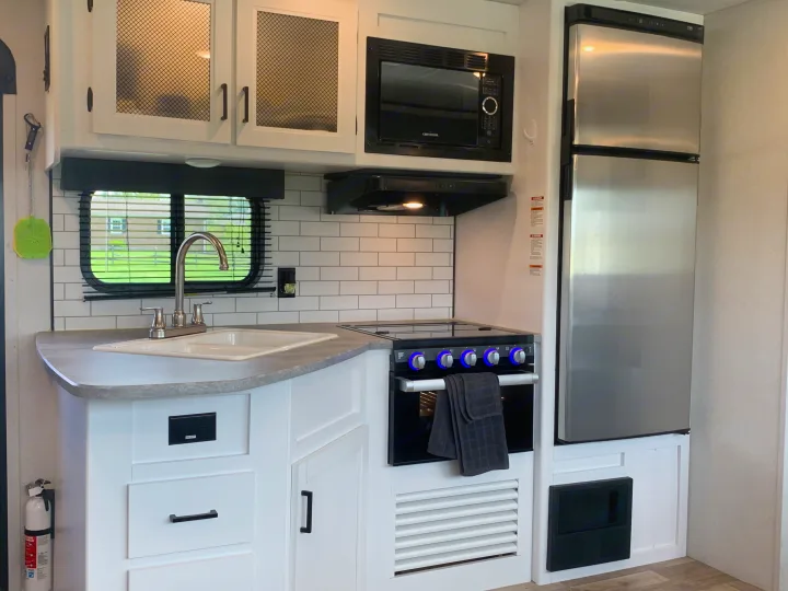 Inside a spacious RV rental kitchen: white cabinets, subway tile backsplash, sink, microwave, oven, and fridge.. Keystone Hideout 2022