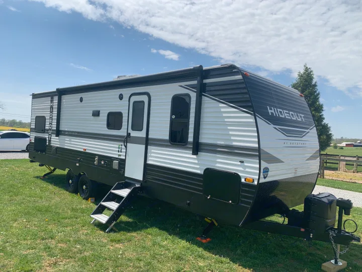 A modern Hideout travel trailer, great for an rv rental, is parked on lush green grass under a bright sky.. Keystone Hideout 2022