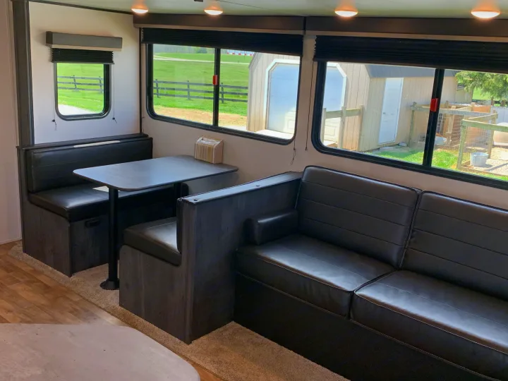 Spacious RV rental interior featuring a cozy dinette, sofa, and large windows with outdoor views.. Keystone Hideout 2022