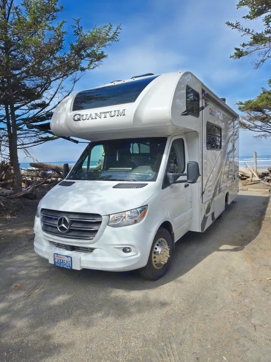 Scenic rv rental: A white Mercedes-Benz Quantum motorhome parked on a Washington beach road, framed by trees.. Thor Quantum 2023