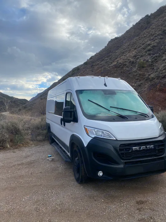 White Ram ProMaster **RV rental** parked on a gravel road in a rugged mountain landscape under a cloudy sky.. RAM ProMaster 2023