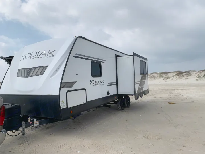 Kodiak Ultra-Lite travel trailer RV rental parked on a sandy beach with dunes under cloudy skies.. Dutchmen Kodiak Ultra Lite 2022