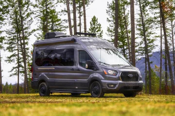 This gray Sanctuary camper van is ready for RV rental adventures in a forest clearing.. Thor Sanctuary 2023