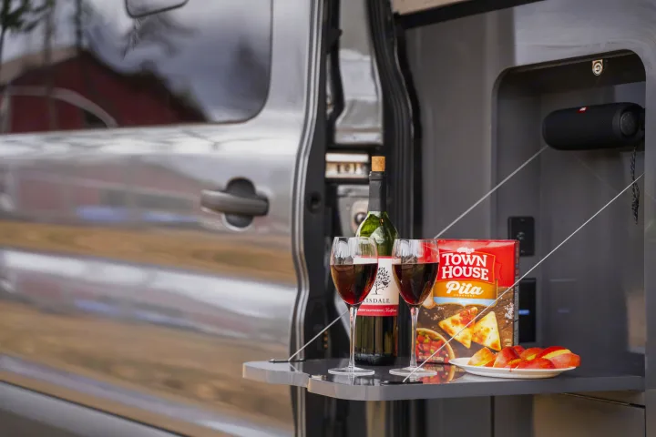 Cozy RV rental setup: wine, crackers, and fruit on a pull-out table for an outdoor picnic experience.. Thor Sanctuary 2023