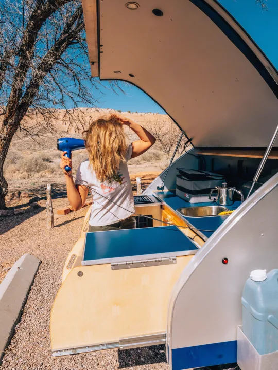 RV rental offers outdoor convenience! Woman dries hair at its compact kitchen in the desert.. Pindrop Travel Trailer Fina Roma 2022
