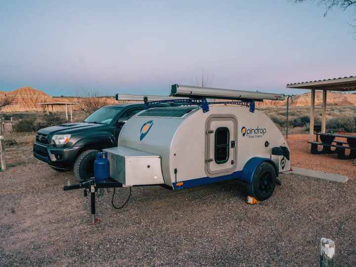 Teardrop RV rental camper and truck at a desert campsite, featuring hills and a picnic area.. Pindrop Travel Trailer Fina Roma 2022
