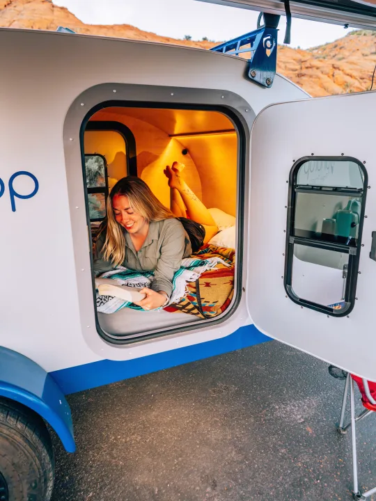 Cozy Roop RV rental: A woman relaxes, reading inside her comfortable teardrop camper amid scenic hills.. Pindrop Travel Trailer Fina Roma 2022