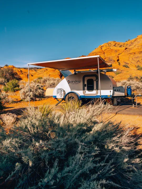 Pindrop teardrop RV rental with awning extended in a vibrant desert campsite, featuring orange rock formations.. Pindrop Travel Trailer Fina Roma 2022