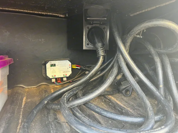 RV rental utility bay showing shore power plugged into a wall inlet, a Lippert slide-out controller, and coiled power cables.. Thor Chateau 2019