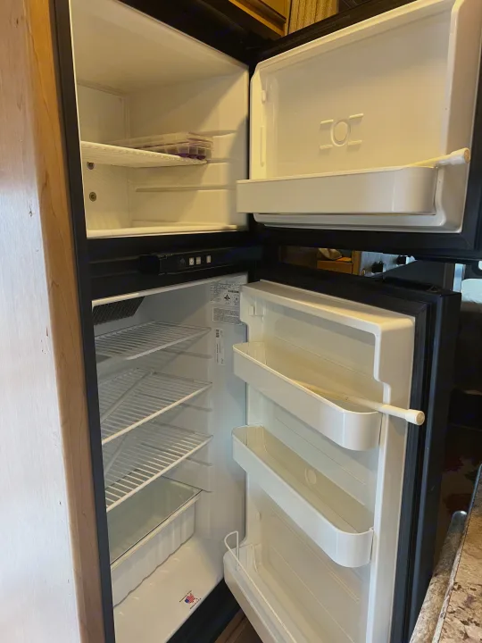 Open, clean RV rental refrigerator, featuring separate freezer and fridge compartments with empty shelves, ready for use.. Thor Chateau 2019