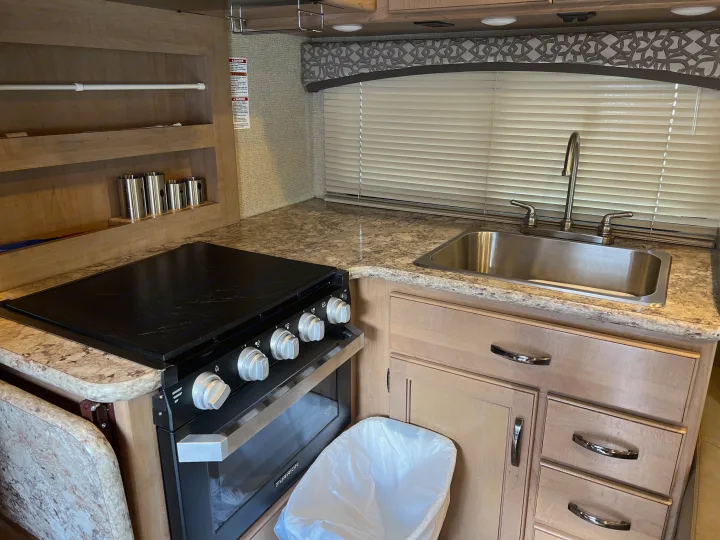 RV rental kitchen: stove/oven, sink, wood cabinets, & blinds. Compact and functional for on-the-go meals.. Thor Chateau 2019