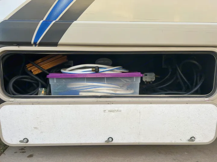 Essential hoses, power cords, and wooden leveling blocks are organized in this RV rental's side storage compartment.. Thor Chateau 2019