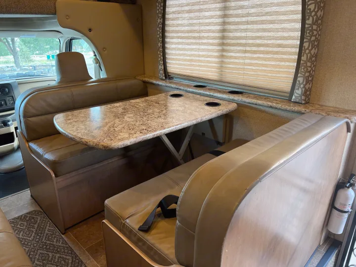 An RV rental's dinette area, featuring a functional table with cup holders, plush seating, and a window.. Thor Chateau 2019