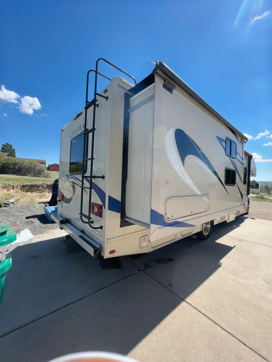 Beige RV rental with an extended side slide-out and rear ladder, parked on a sunny day for your next travel adventure.. Thor Chateau 2019